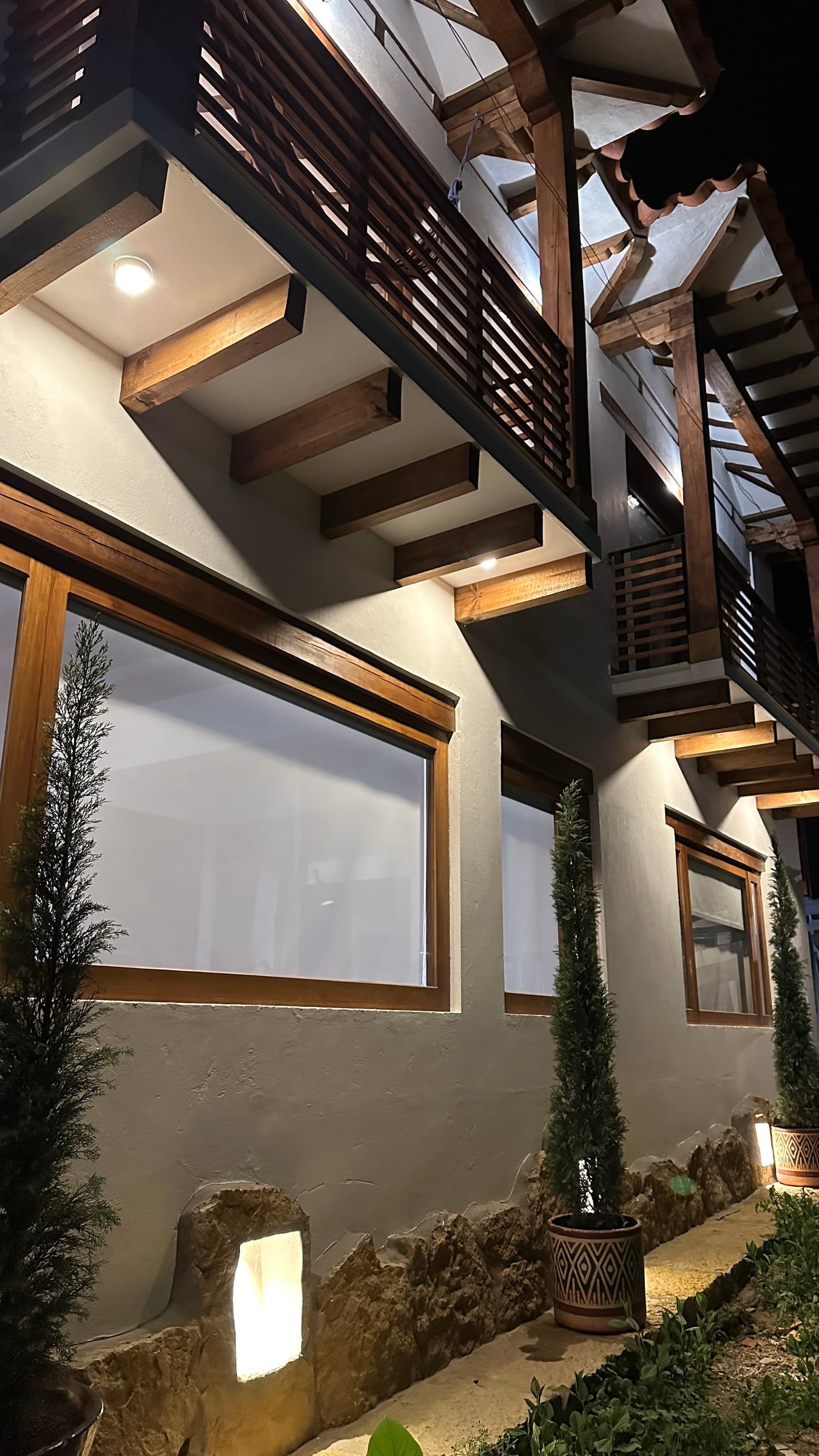 Acceso de la Casa Juan de noche, con balcones de madera y vegetación