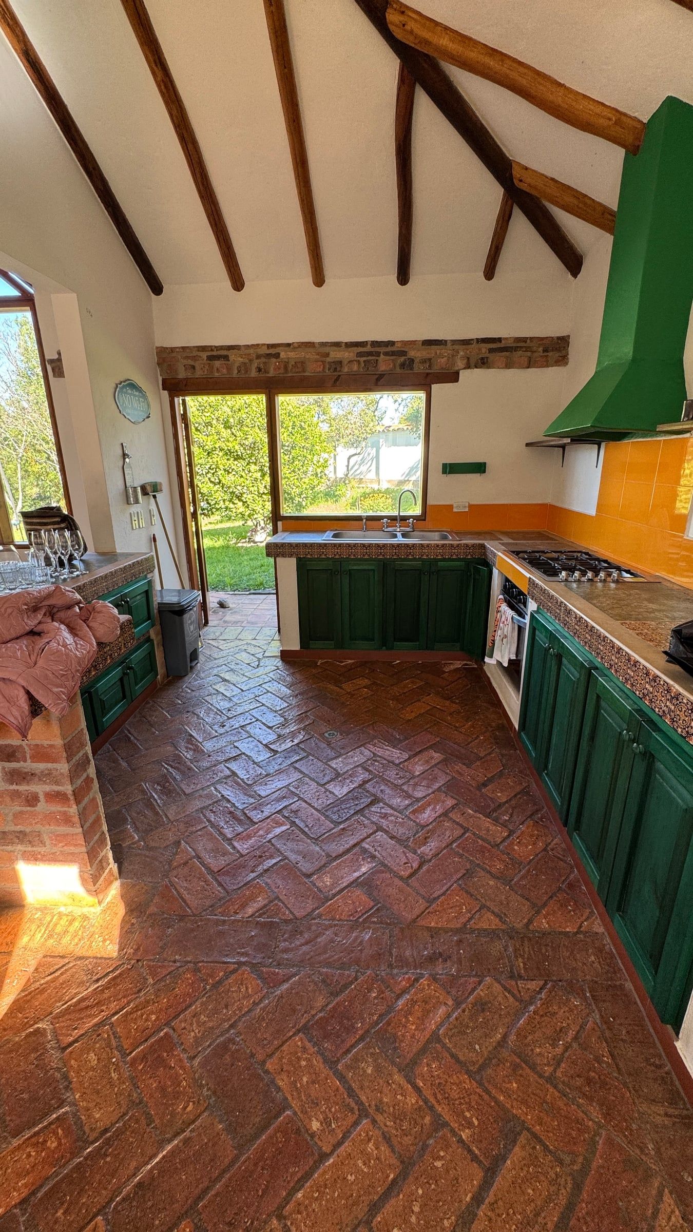 Casa Nido Verde antes de la remodelación: cocina con muebles verdes de obra, piso de ladrillo en espina de pez y cubierta de vigas de madera