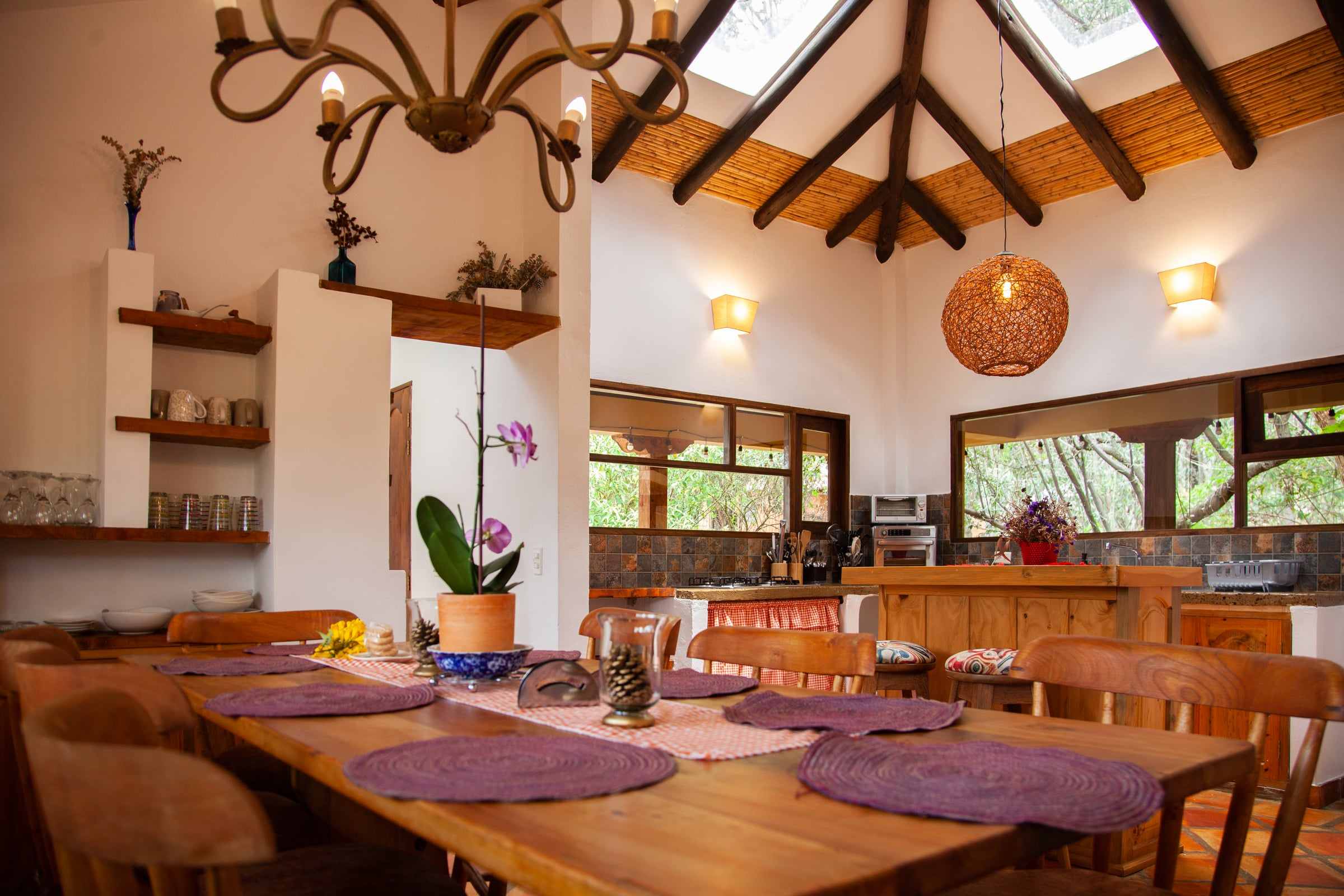 Comedor de Clavellino House bajo una cubierta de madera con claraboyas, con mesa de madera y ventanales hacia el jardín